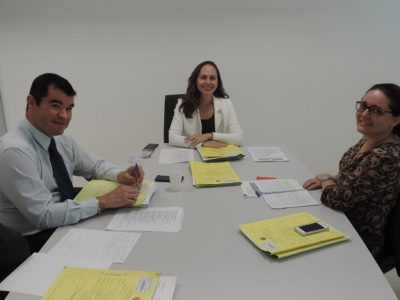 Três Promotores de Justiça em torno de uma mesa sobre a qual há vários processos.
