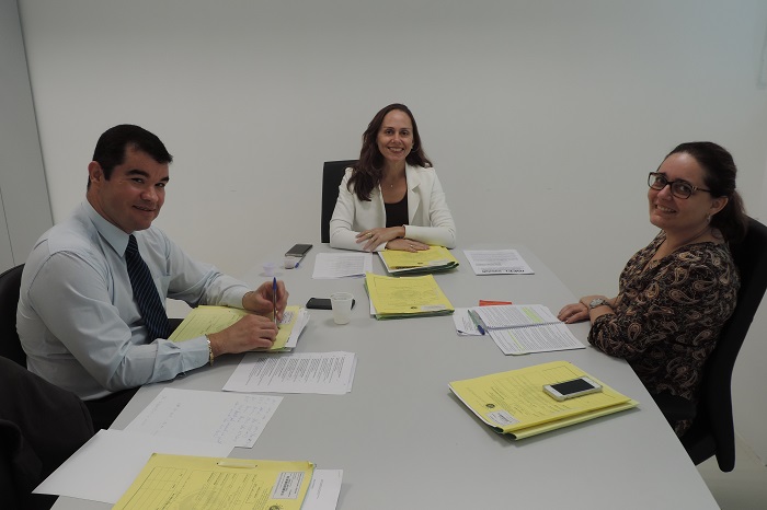 Três Promotores de Justiça em torno de uma mesa sobre a qual há vários processos.