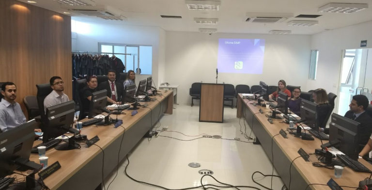 Pessoas ao redor de mesa em U, operando computadores.
