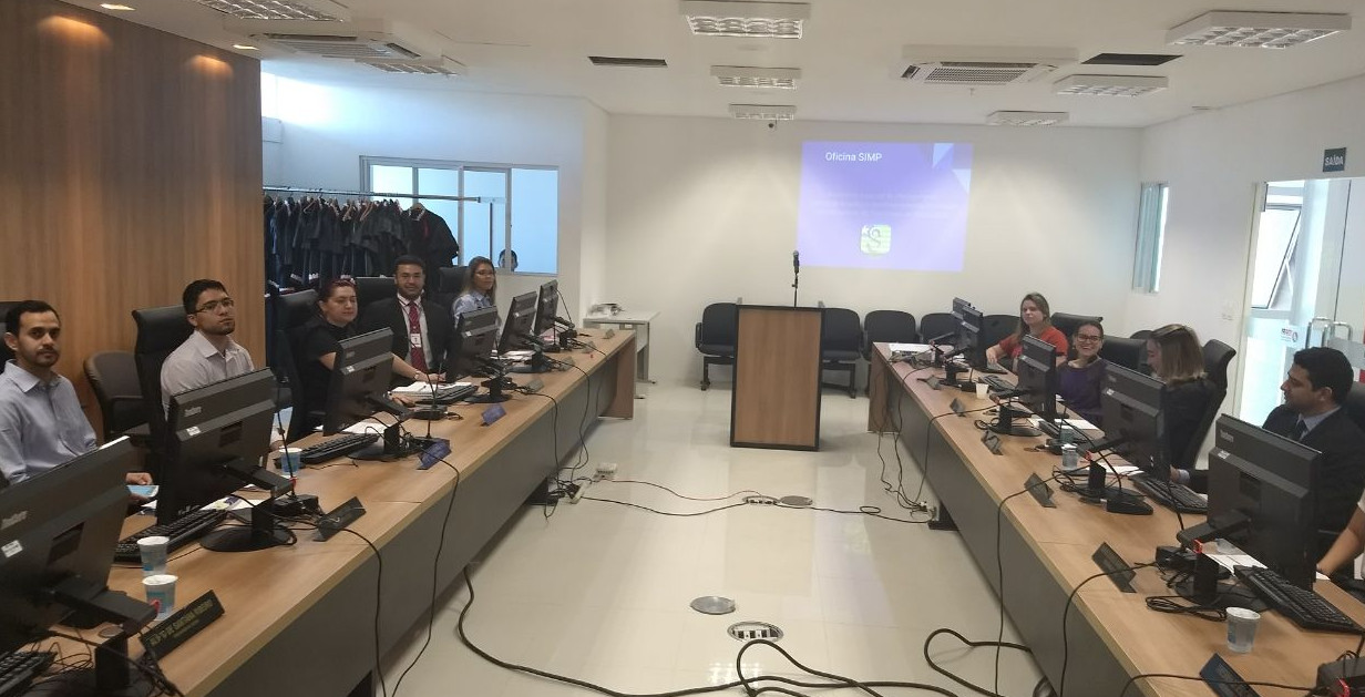 Pessoas ao redor de mesa em U, operando computadores.