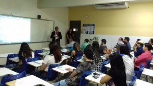 Homem de pé gesticulando, enquanto as demais pessoas estão sentados, observando a explicação