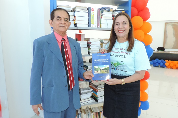 Duas pessoas segurando um livro e sorrindo para fotografia 