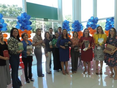 Pessoas segurando livros, posando com uma estante, em um ambiente adornado com balões.
