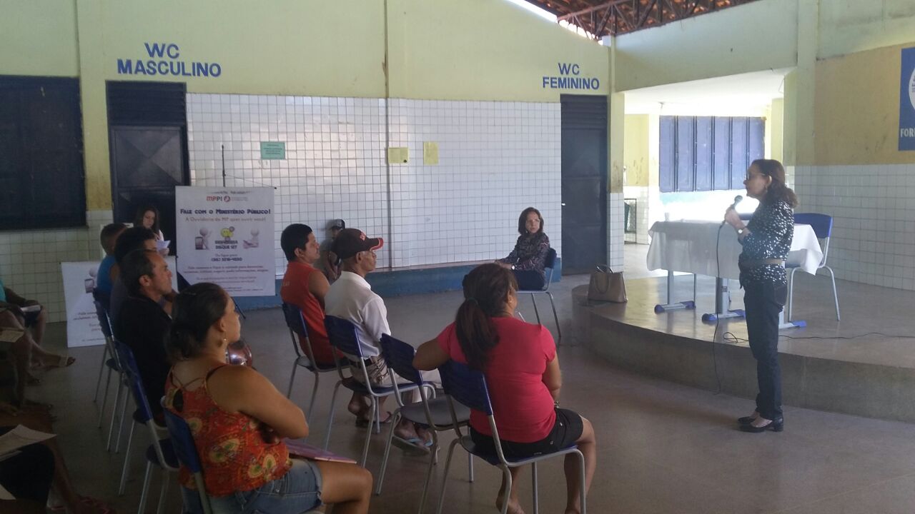 Procuradora de Justiça fala para algumas pessoas sentadas em cadeiras, no pátio de uma escola.