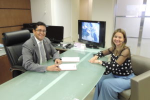 Procurador-Geral de Justiça assinando documentos em sua mesa de trabalho. Sentada à sua frente, está a Assessora Especial de Planejamento e Gestão, Itanieli Rotondo.