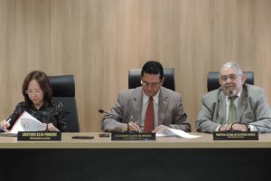 Procurador-Geral assinando documento e mais duas pessoas ao lado
