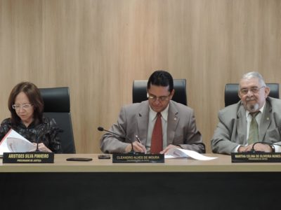 Procurador-Geral assinando documento e mais duas pessoas ao lado