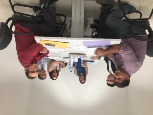 Pessoas sentadas em volta de uma mesa, no momento estão olhando para que está fazendo um fotografia