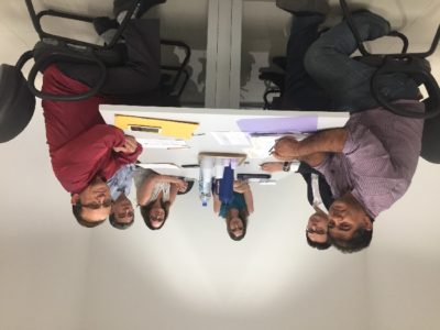 Pessoas sentadas em volta de uma mesa, no momento estão olhando para que está fazendo um fotografia
