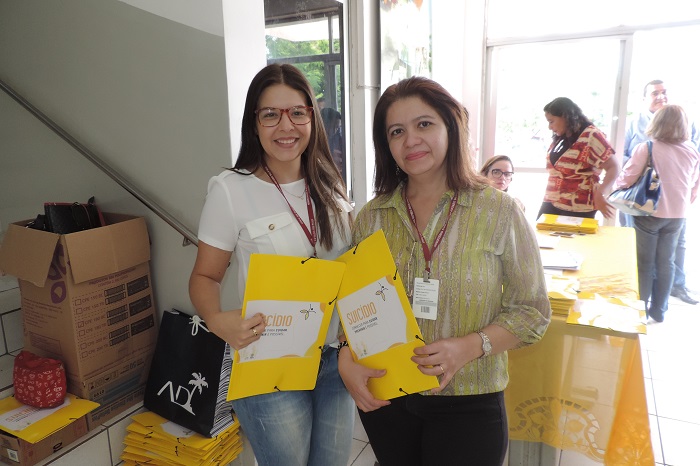 Duas mulheres de pé sorrindo para a fotografia, nas mãos as duas segurança pasta 