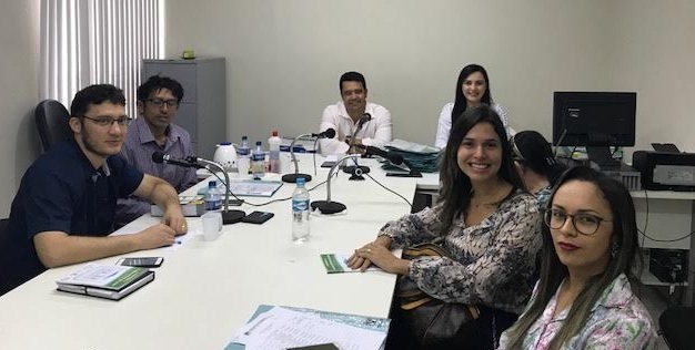 Pessoas sentadas em mesas, durante audiência. No momento estão todos sorrindo e olhando para fotografia