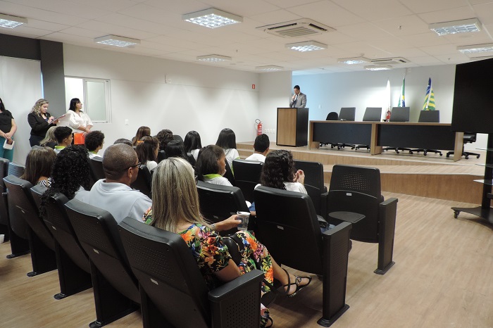 Pessoas sentadas no auditório, observam um homem de pé falando 