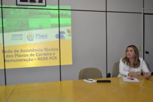 A Promotora de Justiça Flávia Gomes Cordeiro está falando para um público. Atrás dela, há um slide projetado na parede.