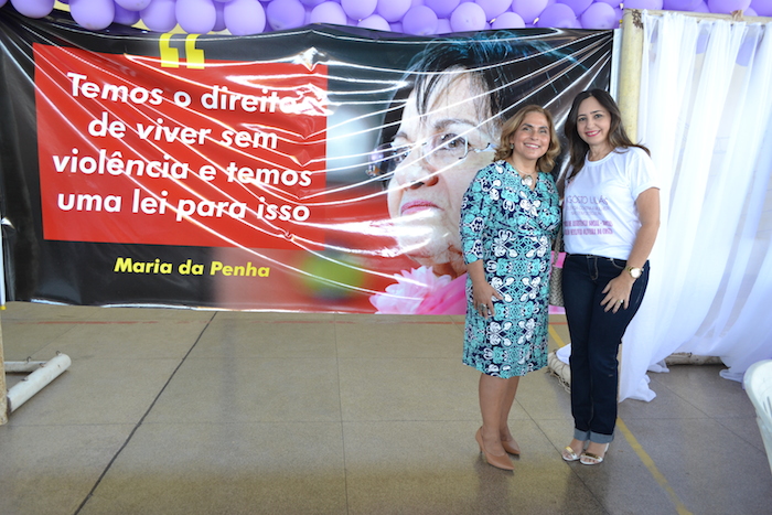Promotora de Justiça posa diante de banner com a foto de Maria da Penha