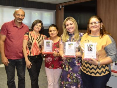 Promotora Flávia Cordeiro e um grupo de pessoas seguram placas de homenagem