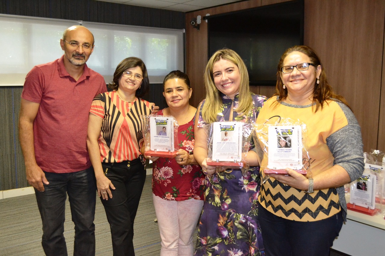 Promotora Flávia Cordeiro e um grupo de pessoas seguram placas de homenagem