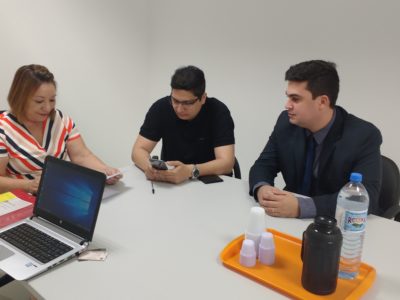 Três pessoas assinam documentos sentadas em torno de uma mesa