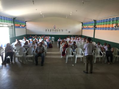 Pessoas sentadas em um ginásio observando a palestra que está sendo proferida