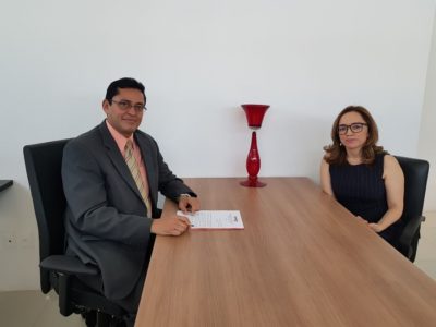 Duas pessoas sentadas em torno de uma mesa. Uma das pessoas segura uma caneta com um documento
