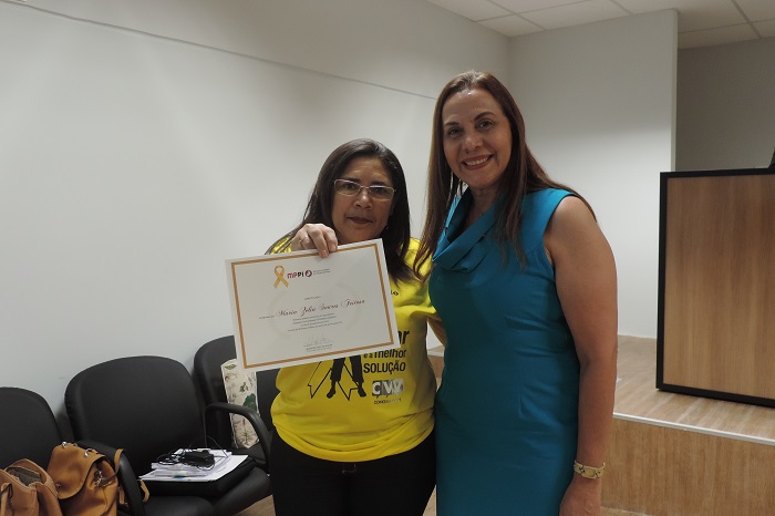 Duas pessoas de pé, uma das pessoas segura um certificado com uma das duas mãos 