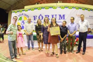 Pessoas de pé e sorrindo. Uma das pessoas segurança um cheque em suas mãos