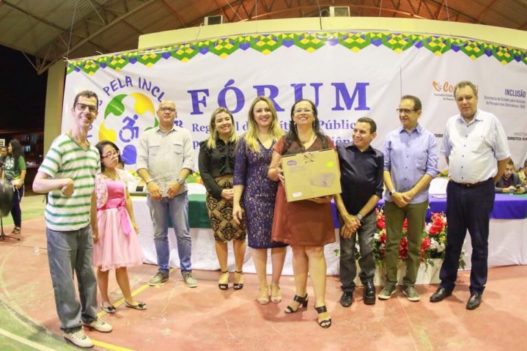 Pessoas de pé e sorrindo. Uma das pessoas segurança um cheque em suas mãos
