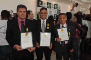 Três pessoas de pé com diploma nas mãos simbolizando a premiação
