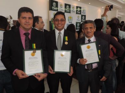 Três pessoas de pé com diploma nas mãos simbolizando a premiação