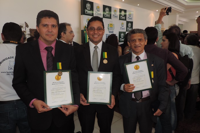 Três pessoas de pé com diploma nas mãos simbolizando a premiação