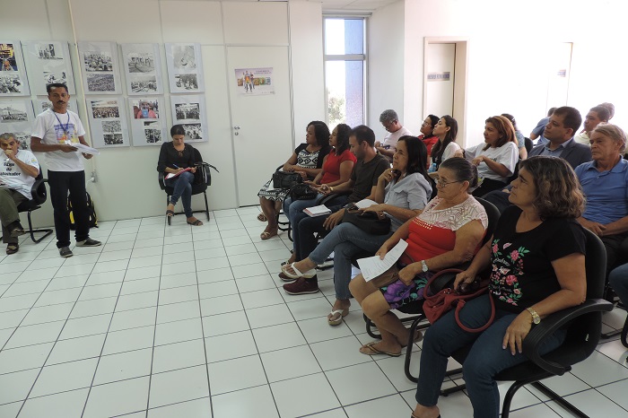 Pessoas sentadas observando um homem que está de pé falando 