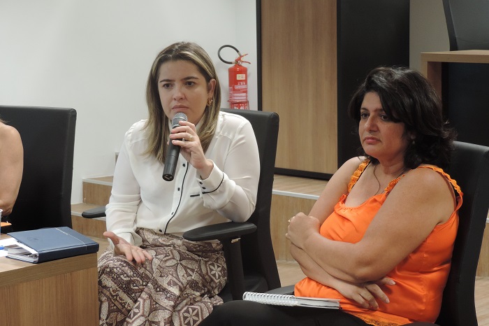 Duas pessoas sentadas, uma das pessoas segura um microfone na mão enquanto fala 