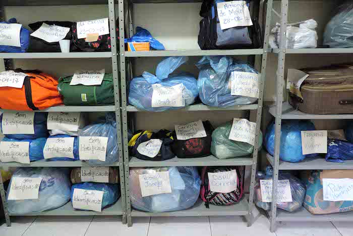 Materiais das pessoas acolhidas pelo Centro Pop. Pacotes acomodados em estantes.