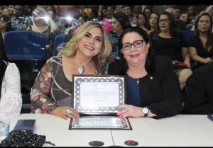Duas mulheres sentadas em uma mesa. As duas segura uma placa
