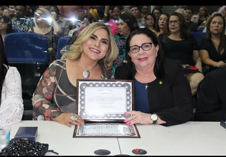 Duas mulheres sentadas em uma mesa. As duas segura uma placa