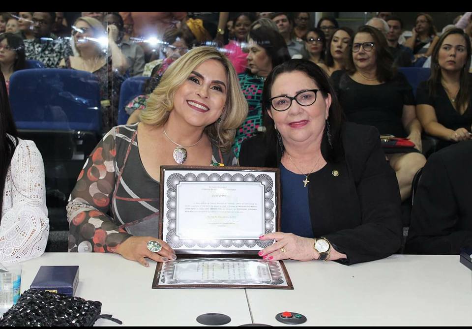 Duas mulheres sentadas em uma mesa. As duas segura uma placa 