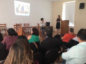 Pessoas sentadas em auditório olhando para outras duas pessoas que estão mais a frente falando sobre o projeto