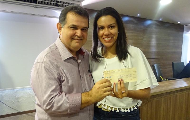 Duas pessoas de pé abraçadas segurando um envelope com as mãos 