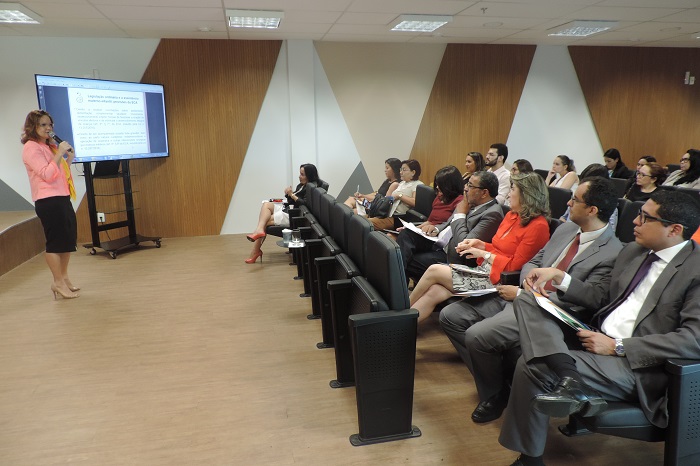 Pessoas sentadas observando uma mulher que está de pé falando 