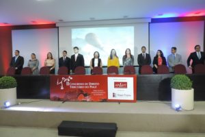 Pessoas de pé sorrindo para fotografia. Estão atrás de uma mesa