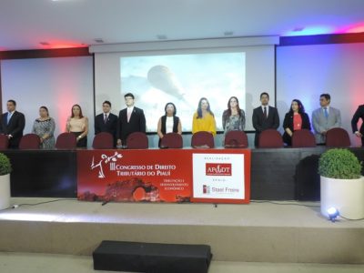 Pessoas de pé sorrindo para fotografia. Estão atrás de uma mesa