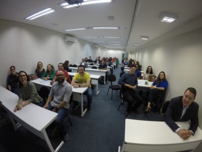 Pessoas divididas em duplas sentadas em várias mesas. Essas pessoas estão sorrindo e olhando para pessoa que faz a fotografia delas