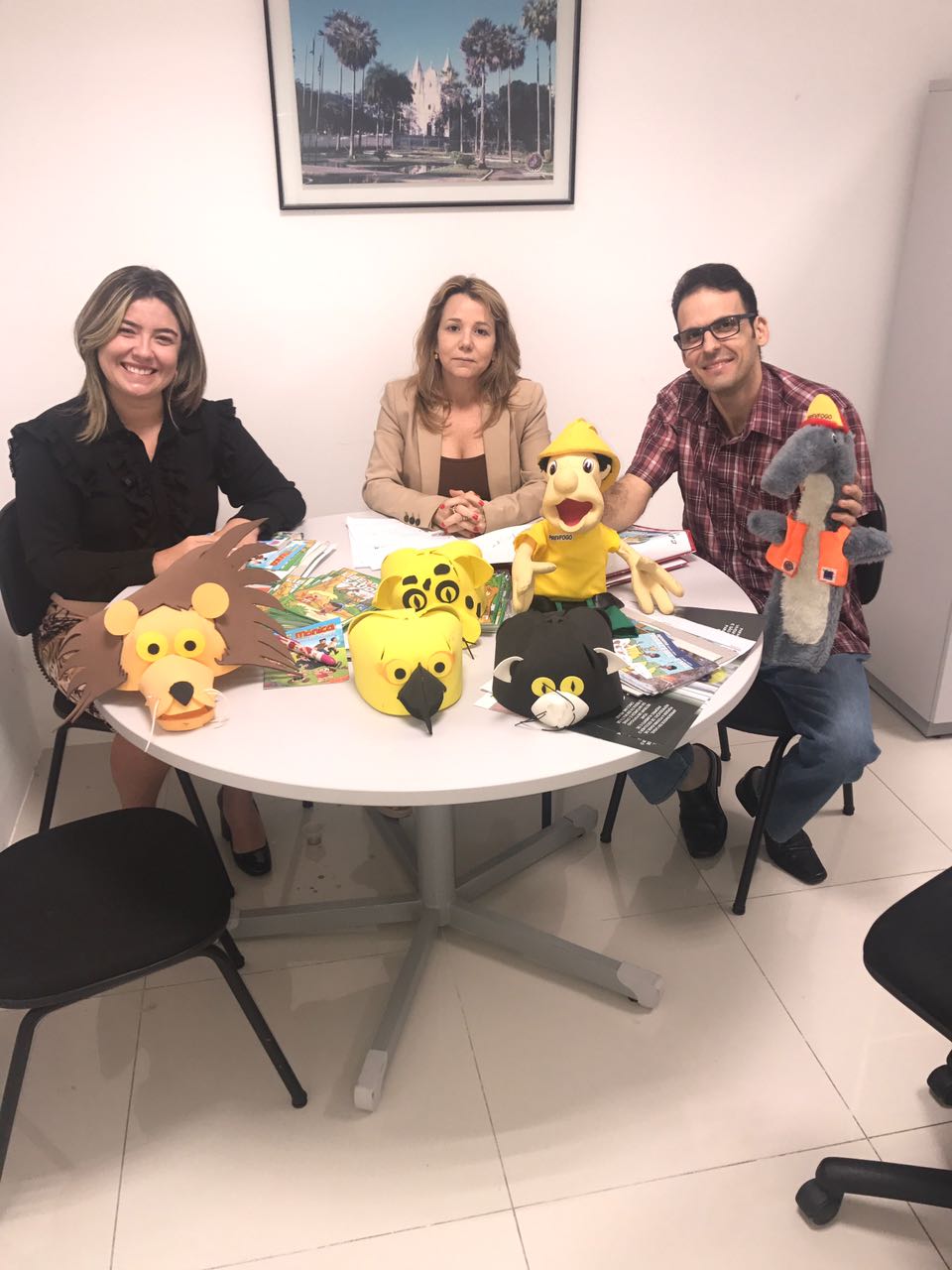 Duas Promotoras de Justiça e um servidor do IBAMA sentados. Na frente deles, em uma mesa, há vários fantoches representando animais.