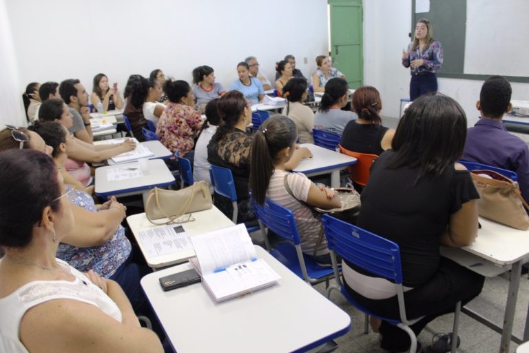 Professores reunidos em uma sala de aula, ouvindo exposição da promotora Flávia Gomes
