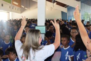 Promotora diante de plateia formada por estudantes
