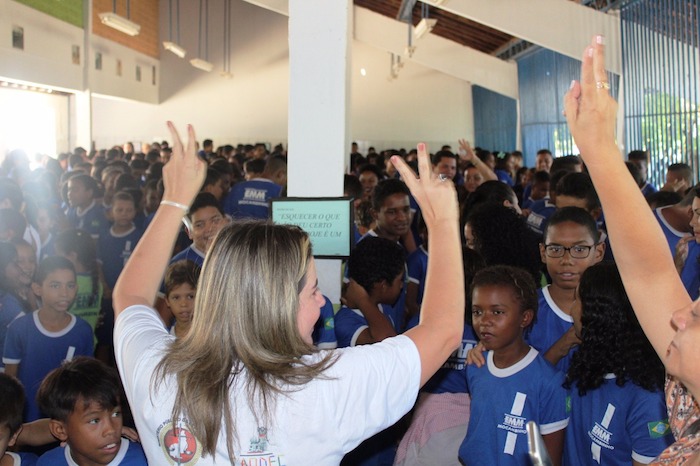Promotora diante de plateia formada por estudantes