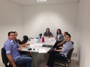 Pessoas reunidas em torno de uma mesa, sob a coordenação da Promotora de Justiça Maria das Graças do Monte Teixeira.