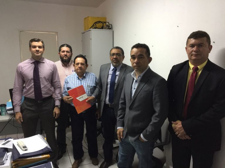 Seis pessoas de pé dentro de um escritório. Uma das pessoas segura um documento