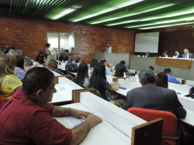 Pessoas sentadas olhando uma mulher que fala