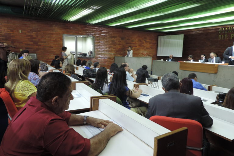 Pessoas sentadas olhando uma mulher que fala