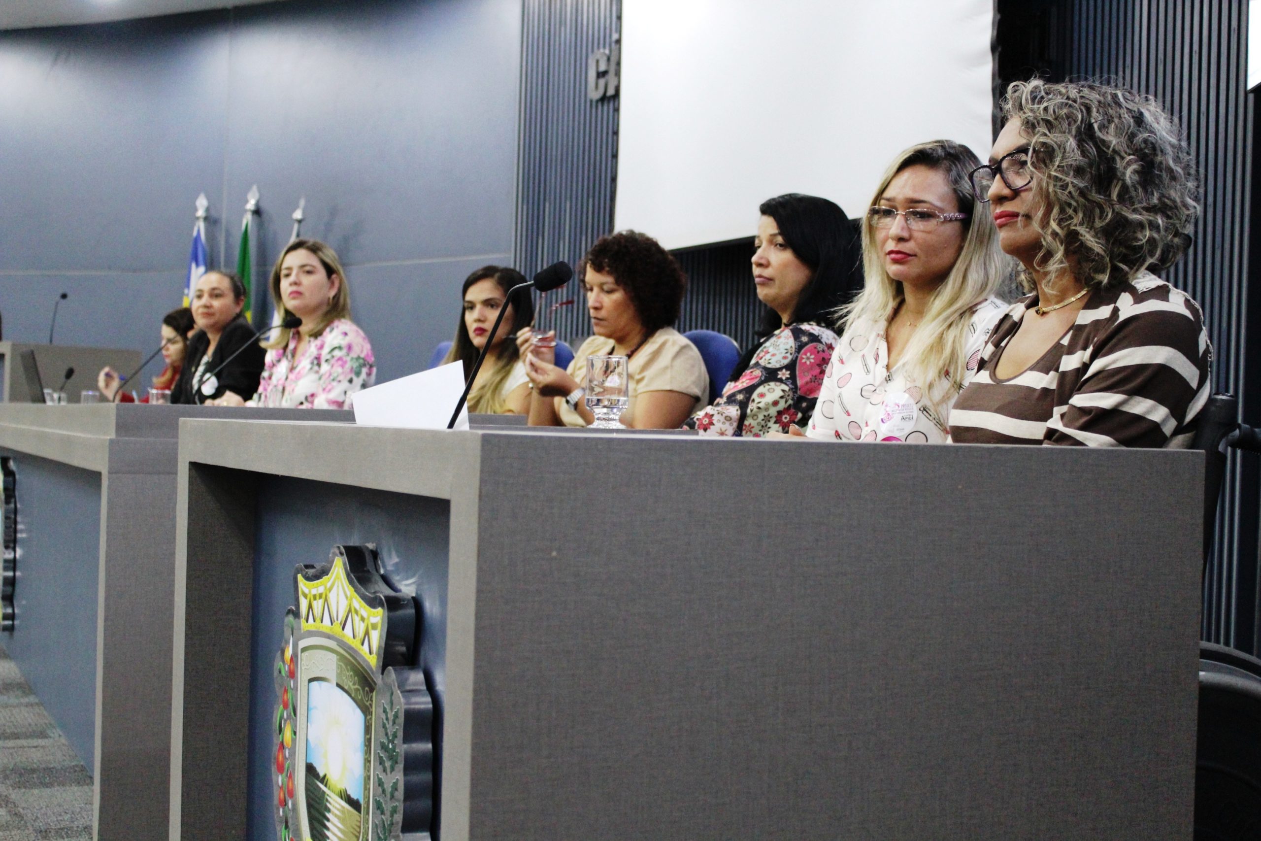 Pessoas sentadas em uma bancada olhando para a plateia 